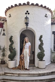 a woman standing in front of a white building with two dogs sitting on the steps