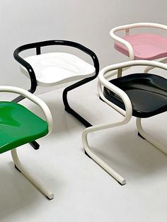 three different colored chairs sitting next to each other on a white surface with black, pink, and green