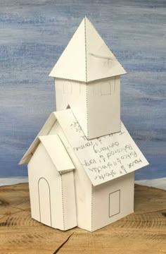 a paper model of a church with writing on the front and side walls, sitting on a piece of wood