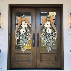 two wreaths on the front door of a house decorated with flowers and greenery