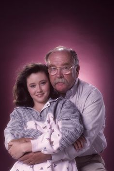 an older man hugging a young woman in front of a purple background with her arms around him