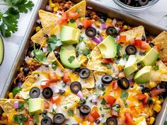 a tray filled with nachos topped with cheese, black olives and avocado