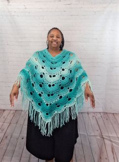 a woman wearing a blue crochet shawl standing in front of a white brick wall