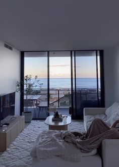 a person laying on a couch in a living room with large windows looking out to the ocean