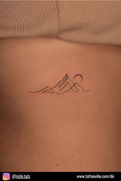 a woman's stomach with a mountain tattoo on her left side ribcage