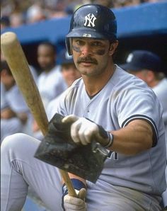 a baseball player holding a bat in his right hand and sitting on the dugout