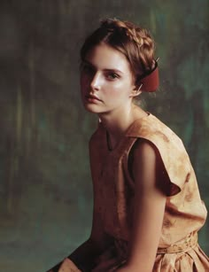 a woman in a dress sitting down with her hand on her hip and looking at the camera