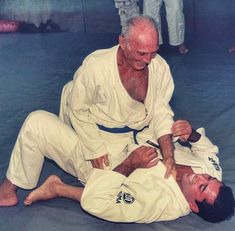 an older man is helping another man with his karate moves on the ground while others look on