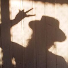 the shadow of a person wearing a cowboy hat on a wooden wall with a skateboard