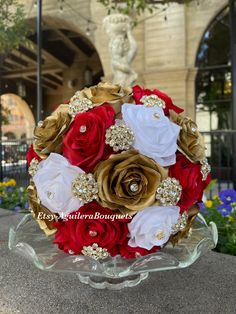 a bridal bouquet with red, white and gold flowers on a glass platter