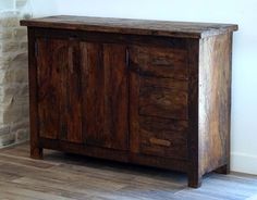 a wooden cabinet sitting on top of a hard wood floor next to a brick wall