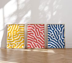 three different colored paintings sitting on top of a hard wood floor next to a white wall