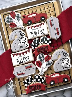 decorated cookies in the shape of race cars on a cookie sheet with red ribbon around them