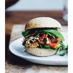 a sandwich with meat, lettuce and tomato on a white plate sitting on a wooden table