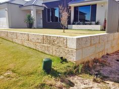 a concrete block wall in front of a house with grass on the ground and trees