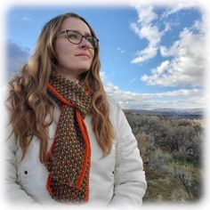 a woman wearing glasses and a scarf looks off into the distance while standing on top of a hill