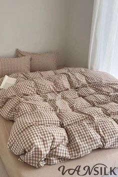 an unmade bed with brown and white checkered comforter on it in front of a window