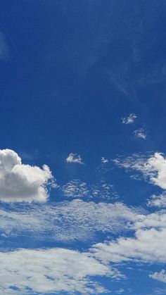 the airplane is flying high in the blue sky with white fluffy clouds and some green grass