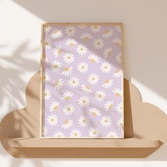 a wooden shelf with a purple and white flowered print on the wall next to a potted plant