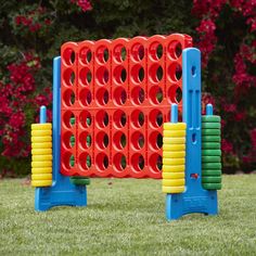 an orange and blue plastic game set in the middle of some grass with red flowers behind it