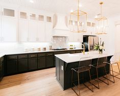 a kitchen with black cabinets and white counter tops, gold accents on the pendant lights over the island