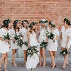 a group of women standing next to each other wearing white dresses and holding bouquets