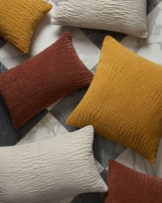 four different colored pillows sitting on top of a marble floor next to an orange and white pillow