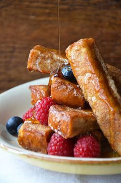 french toast with berries and syrup being drizzled over it on a plate