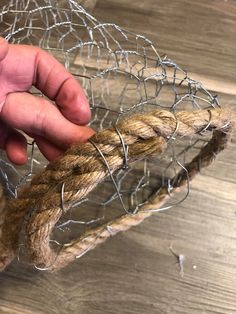 a hand holding a piece of rope that is attached to a wire mesh basket on top of a wooden table