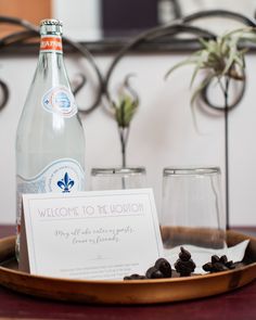 a bottle of water sitting on top of a wooden tray next to two glasses and a sign