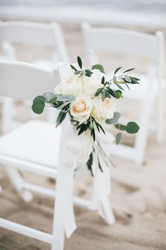 a bouquet of white roses and greenery is tied to a chair on the beach