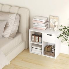 a bed with white sheets and pillows next to a small book shelf filled with books