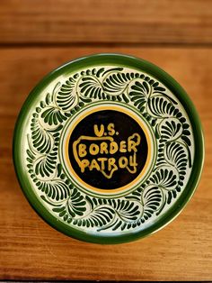 a green and yellow plate with the words us border patrol on it sitting on a wooden table