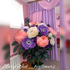 a vase filled with flowers on top of a table next to a window covered in purple curtains