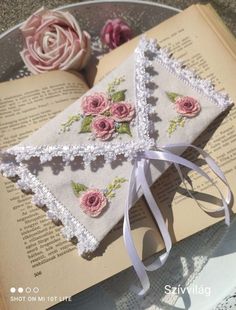 an open book with pink roses on it and white ribbon tied around the edge, sitting on top of a table