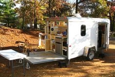 a white trailer parked in the woods with its door open and shelves on it's side