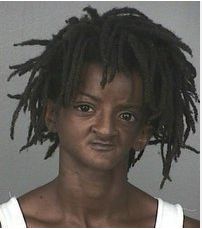 a mug shot of a man with dreadlocks on his head and chest, wearing a white shirt