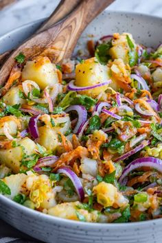 a salad with potatoes, onions and carrots in a white bowl next to a wooden spoon