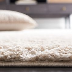 a close up view of a white rug on the floor with pillows in the background