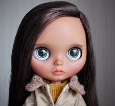 a close up of a doll with long hair and blue eyes wearing a trench coat