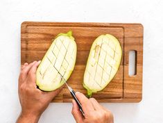 a person cutting an eggplant on a wooden cutting board with a pair of scissors