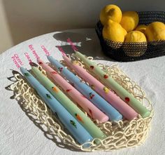 five different colored candles sitting on top of a table next to lemons and a basket