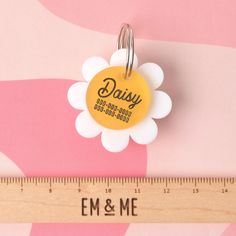 a yellow daisy shaped badge sitting on top of a measuring ruler next to a pink and white wall