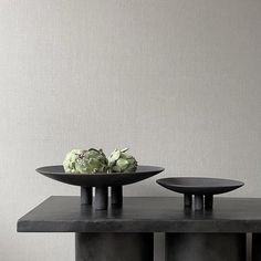 two black plates with flowers on them sit on a table in front of a gray wall