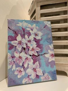 an acrylic painting of pink and white flowers on a blue background, sitting on a table