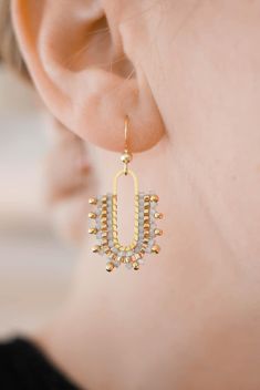 a close up of a person wearing earring with gold and white beads on it