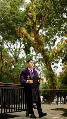 a man in a graduation gown is standing on a bench with his hands folded up