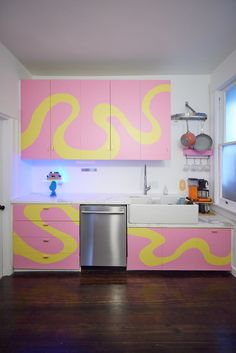 a kitchen with pink and yellow cabinets, stainless steel dishwasher, and sink