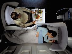 two people are sitting on an airplane with food in the trays, and one person is eating