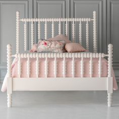 a white bed with pink pillows on top of it and some gray walls behind it